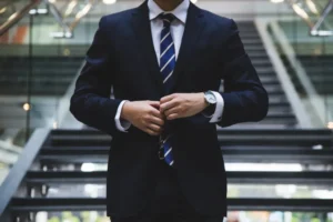 A man in a smart suit adjusting his jacket in a professional setting.